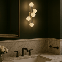 Alabaster Alba wall sconce glowing above a marble bathroom vanity in a luxury interior.