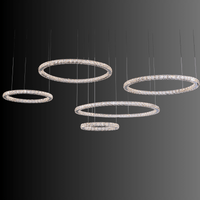 Five radiant crystal rings forming a modern chandelier suspended against a dark background, showcasing LED illumination.