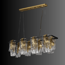 Aurora Magma linear brass chandelier with clear and gold Murano-style glass panels suspended against a dark contemporary backdrop.