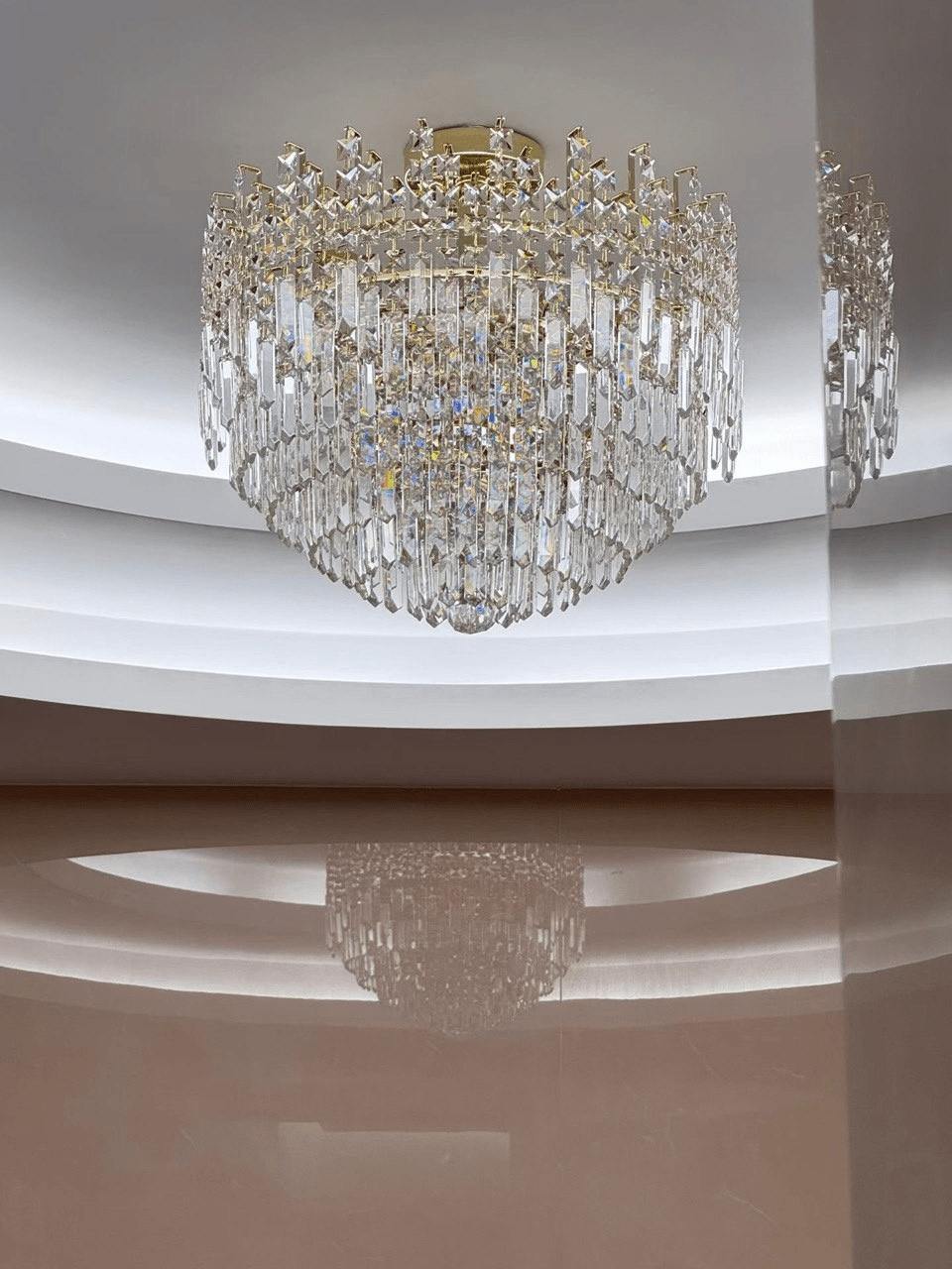 Maurice Doré gold crystal chandelier installed on a modern ceiling, illuminating the space with warm light and layered crystal reflections.