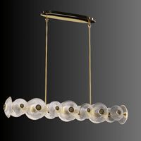 Modernus Linear chandelier illuminated on a dark background, showcasing sculpted Murano-style glass discs and brass-gold.