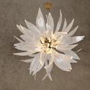 Murano-style Helios sunburst chandelier with hand-forged glass blades and copper frame, illuminated in warm light against a neutral wall.