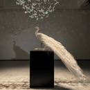 Crystal peacock sculpture beneath luxury chandelier, showcasing scale and presence in refined interior.