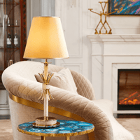 Maria Eleganza gold and Asfour crystal table lamp styled in a luxury interior beside a sofa and decorative florals.
