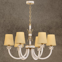 Maria Petite Éclat 6-light gold crystal chandelier with ivory shades and Asfour crystal arms shown a textured grey wall.