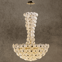 Luxury Modernus Grande chandelier with sculpted Murano-style glass discs and brass-gold frame, on a stone backdrop.