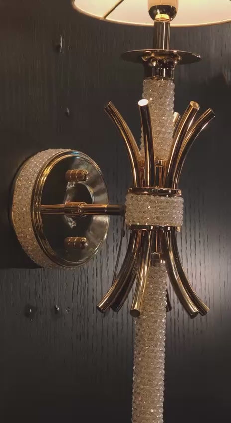 Maria Sconce Élan gold and crystal wall light glowing softly in a dim interior, highlighting its sculptural 18K gold-plated design.