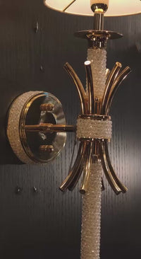 Maria Sconce Élan gold and crystal wall light glowing softly in a dim interior, highlighting its sculptural 18K gold-plated design.