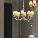 Maria Petite Éclat chandelier glowing in a dimly lit interior, featuring six ivory shades, crystal accents and 18K gold-plated arms.