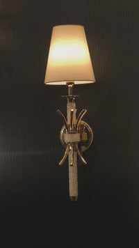 Maria Sconce Élan gold and crystal wall light glowing softly in a dim interior, highlighting its sculptural 18K gold-plated design.