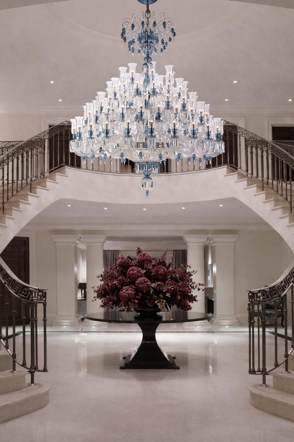Large tiered crystal chandelier installed in a two-story classical foyer with symmetrical staircase for architectural stairwell lighting.