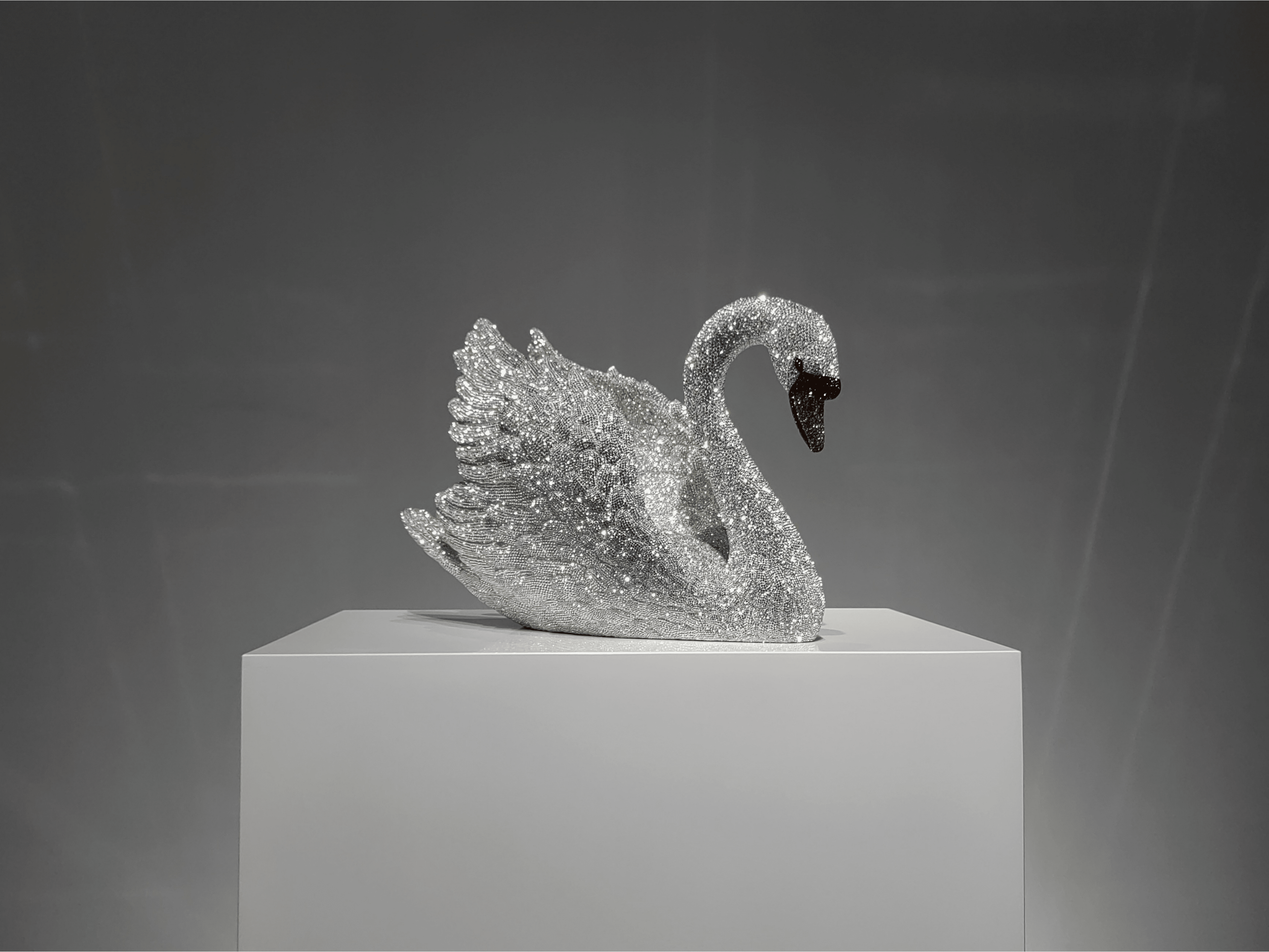 Luxury Swarovski crystal swan sculpture VAGHAAR shown in elegant angled profile on gallery pedestal.