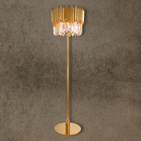Luxury crystal floor lamp in polished 24K gold-plated steel with faceted prism shade on architectural wall