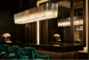 Linear crystal chandelier installed above black marble kitchen island in ultra-luxury interior.